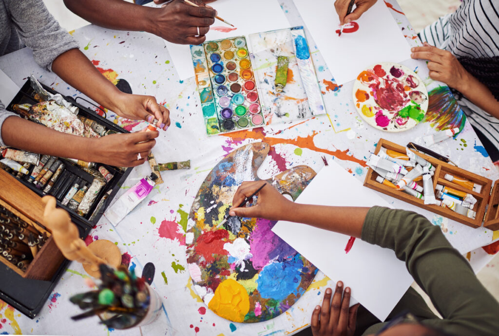 paints and palettes on table with hands holding paint brush